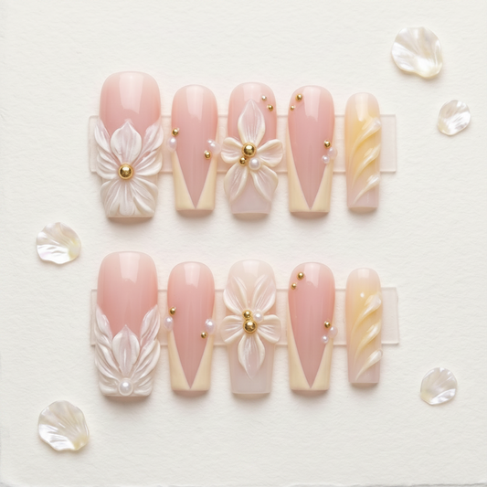 A close-up view focusing on the central index finger nail, showcasing a stunning, hand-sculpted white 3D flower with a precise cluster of gold beads and a pearl. The design is complemented by neighboring pink and cream French tip artificial nails with delicate bead accents