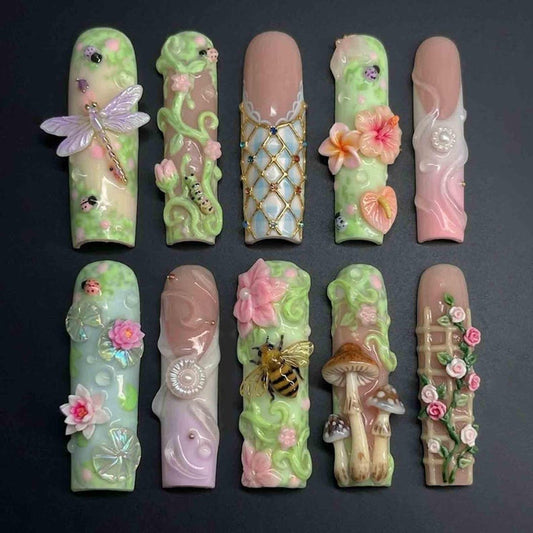 Close-up of hands wearing intricate, maximalist artificial nails featuring tiny ladybugs, pink roses, and woodland details in a fairycore aesthetic.