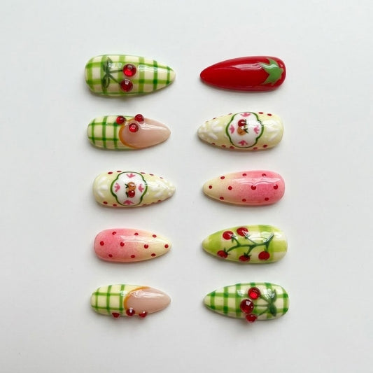 Ten individual almond-shaped press-on nail pieces neatly aligned in two vertical rows against a clean, minimalist white background, highlighting the glossy gel finish, cherry-red tips, and green gingham check patterns.