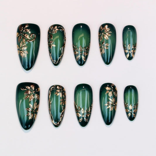 A luxury set of stiletto-shaped reusable false nails in deep jade green, decorated with intricate metallic gold leaf patterns, 3D floral accents, and a glossy gel topcoat, showcased for an online boutique