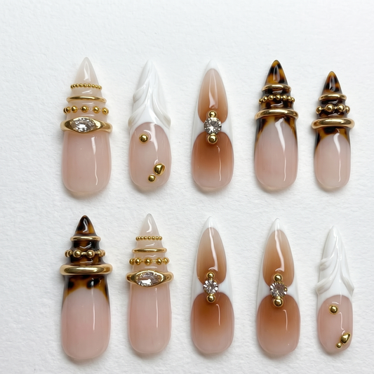 A close-up of an edgy luxury manicure featuring extra-long stiletto fake nails with warm brown gradient ombré and sparkling rhinestone centers.