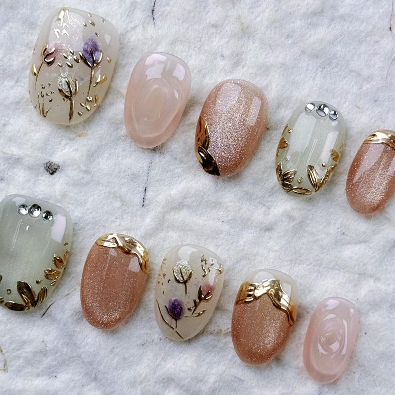 Macro shot of luxury press-on nails highlighting the intricate 3D hand-painted lavender flowers and structured gold chrome charms on a soft gel base.