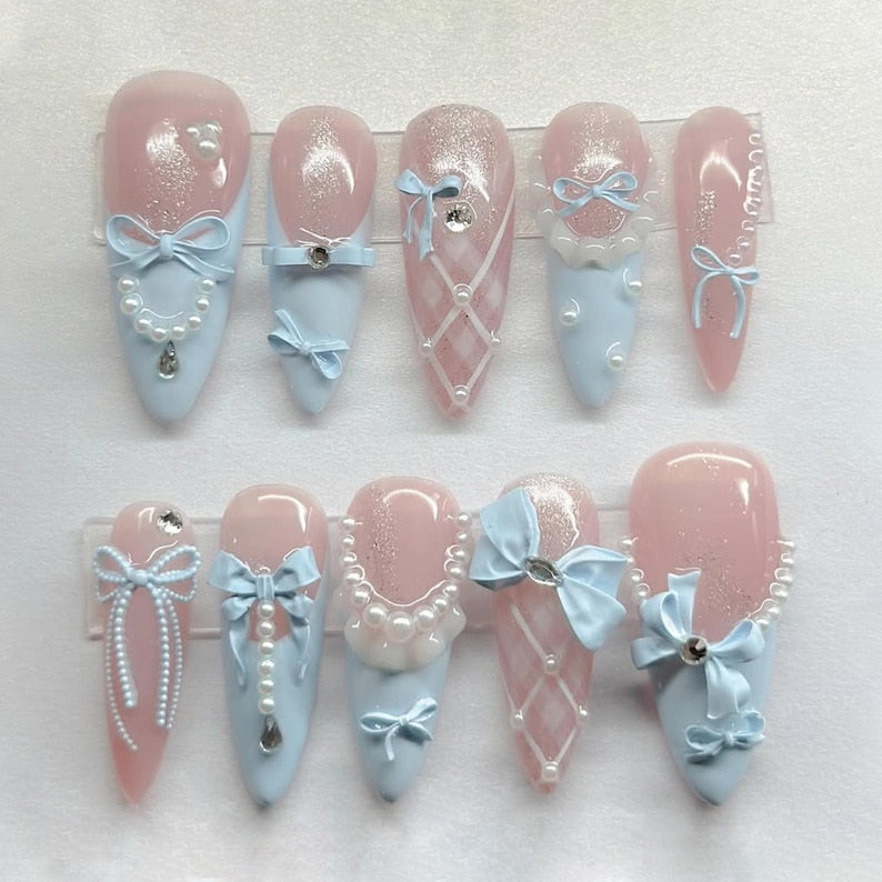 Handmade almond-shaped press-on nails with intricate ribbon charms and elegant pearl jewelry, perfect for a romantic aesthetic.