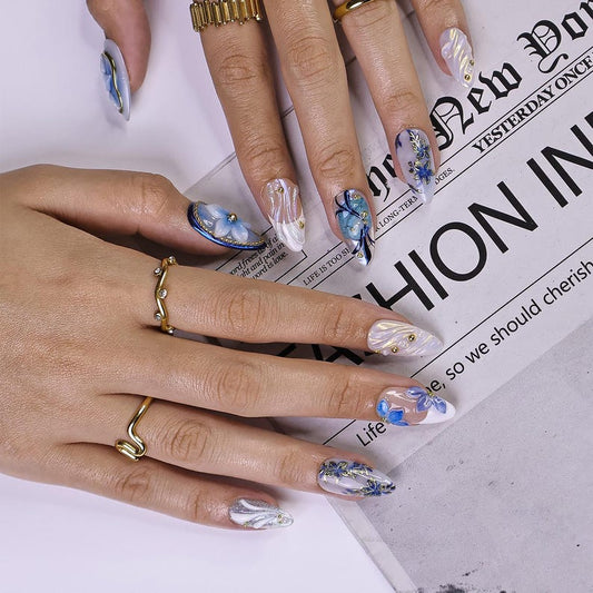 Almond press-on nails with 3D blue flowers, gold outline and pearl beads on icy blue base