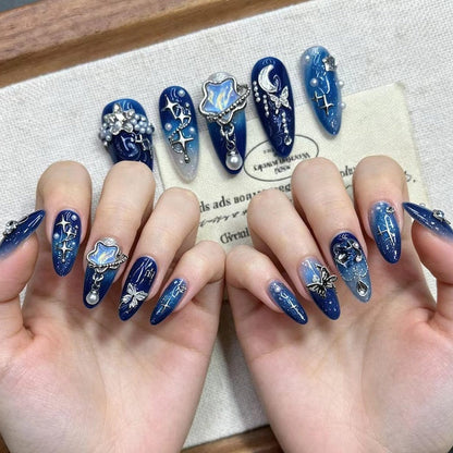 Close-up of 3D butterfly and crescent moon nail art designs on almond-shaped press-on nails in royal blue and silver glitter gradients.