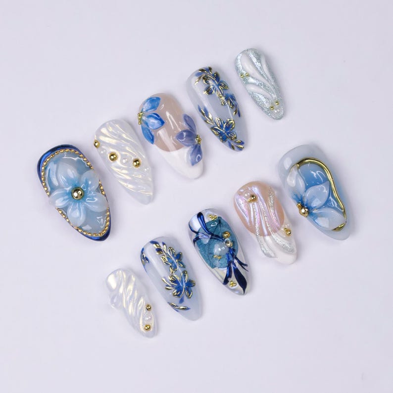 3D raised blue flower nail art with hand-painted gold outline on sheer nude almond press-on nails