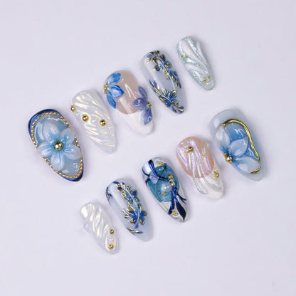 3D raised blue flower nail art with hand-painted gold outline on sheer nude almond press-on nails