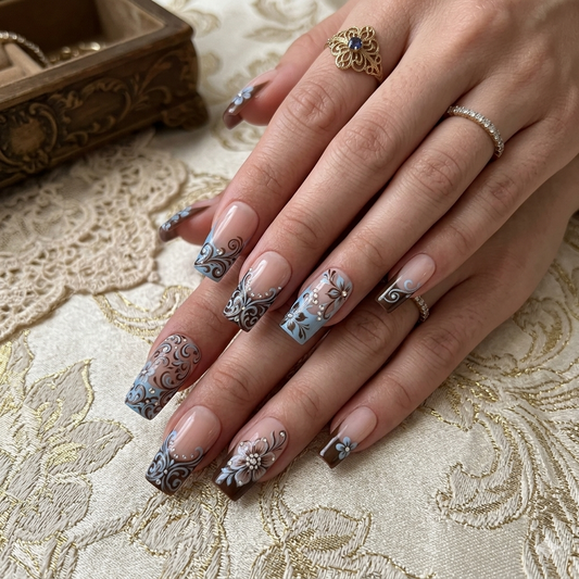 A luxury set of handmade press-on nails featuring vintage baroque swirls, blue floral accents, and intricate 3D rhinestone nail art on a soft nude gel base.
