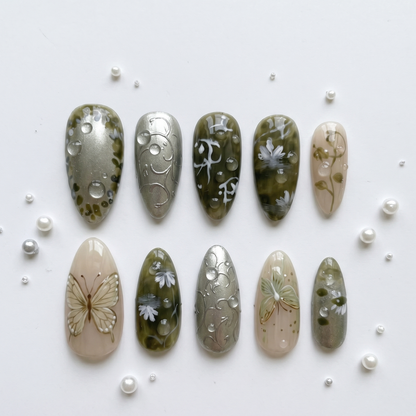 Whimsical sage green press-on nails featuring delicate woodland-inspired butterfly art and realistic water droplet details for an organic look.
