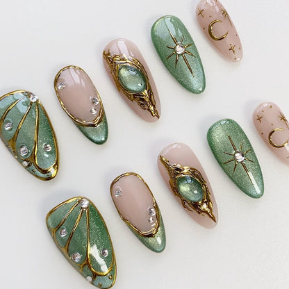 Witchy celestial fake nails with moon star designs, gold accents, and shimmering emerald green cat-eye