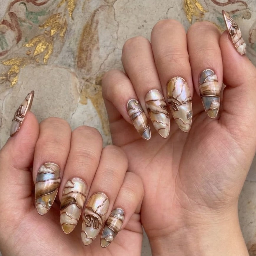 These stiletto-shaped press-on nails feature an exquisite, intricate classical design with marble swirls in brown, cream, and iridescent blue. Copper wire and pearl details add a luxurious touch.