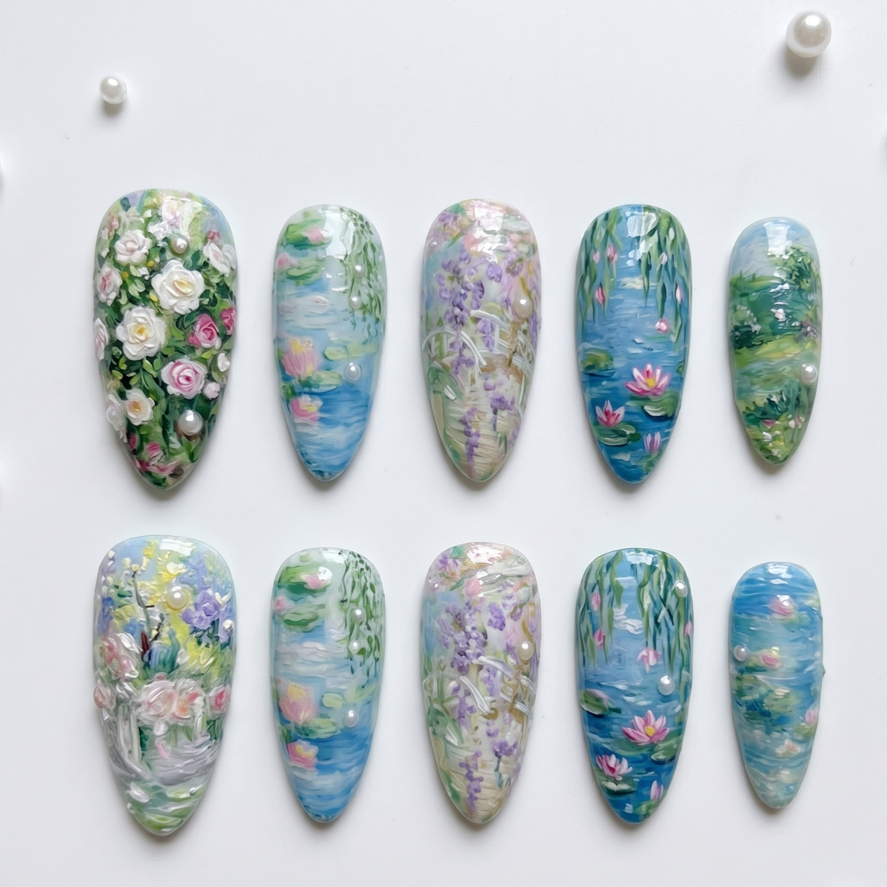 A detailed close-up shot focusing on specific nails within the set, showcasing the textured, painterly brushstrokes and delicate pearl accents on the Monet-inspired pink water lily and green lily pad designs.