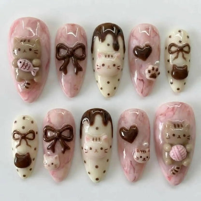 Elegant almond-shaped reusable false nails adorned with intricate 3D kitty paws, yarn balls, and dark chocolate hearts, displayed beautifully against a coordinating pastel pink background.