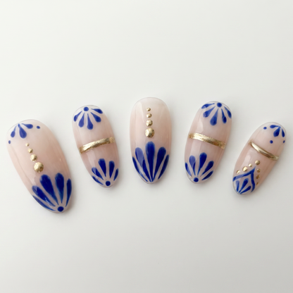 Elegant nude nail art with cobalt blue patterns and gold studs