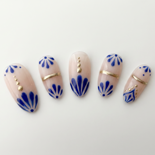 Elegant nude nail art with cobalt blue patterns and gold studs