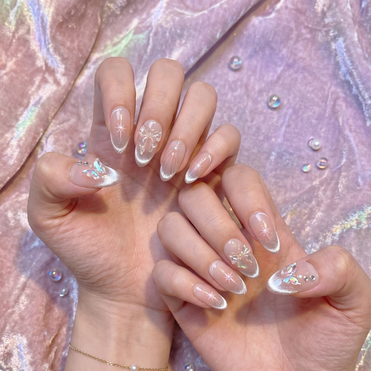 Celestial-inspired almond press-on nails featuring iridescent 3D butterflies, dainty bows, and hand-painted starburst accents on a nude-to-silver gradient by JRNAIL.