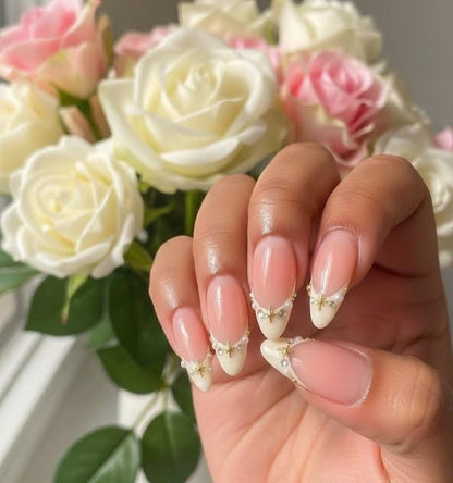 Elegant almond-shaped French tip press-on nails featuring gold celestial charms and pearl accents on a nude base.