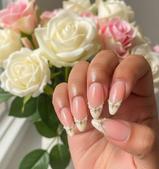 Elegant almond-shaped French tip press-on nails featuring gold celestial charms and pearl accents on a nude base.
