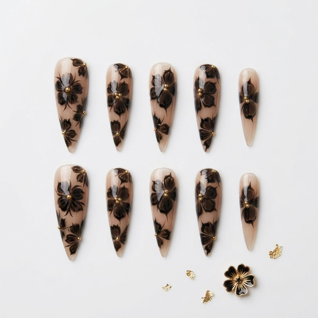 Close-up of long stiletto false nails showcasing a smoky ink-bleed orchid pattern, hand-painted 3D gel textures, and elegant metallic gold embellishments.