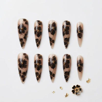Close-up of long stiletto false nails showcasing a smoky ink-bleed orchid pattern, hand-painted 3D gel textures, and elegant metallic gold embellishments.