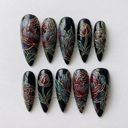 Macro view of intricate hand-painted floral nail art with gold line-work on a deep black background, showcasing high-end craftsmanship in gothic-style press-ons.