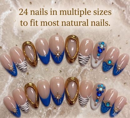 A full 24-piece luxury press-on nail set featuring royal blue French tips, hand-painted zebra stripes, and 3D molten gold textures with star charms laid out on a soft fabric background with text reading '24 nails in multiple sizes to fit most natural nails.
