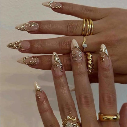 Two rows of ten nude gel press-on nails from JRNAIL on a crisp white background, featuring raised 3D liquid gold chrome filigree, ornamental swirls, and delicate rhinestone crown accents.