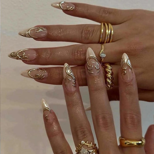 Two rows of ten nude gel press-on nails from JRNAIL on a crisp white background, featuring raised 3D liquid gold chrome filigree, ornamental swirls, and delicate rhinestone crown accents.