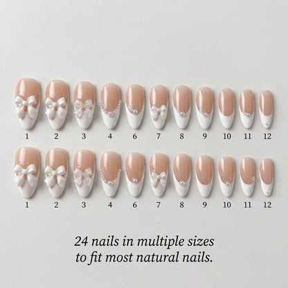 A premium 24-piece luxury press-on nail set featuring sharp stiletto tips with crisp white French manicures and 3D white bow charms, arranged neatly in concentric arches over a textured metallic and light wood background with text reading '24 nails in multiple sizes to fit most natural nails.