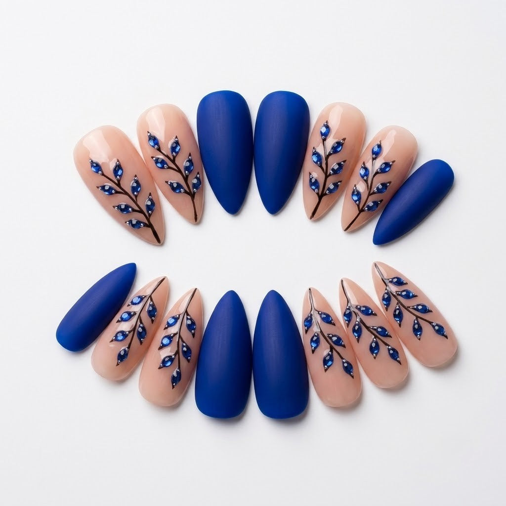 Close-up of handmade botanical false nails showcasing the striking contrast between deep matte cobalt blue layers and intricate sapphire rhinestone leaf clusters set along delicate black vine art