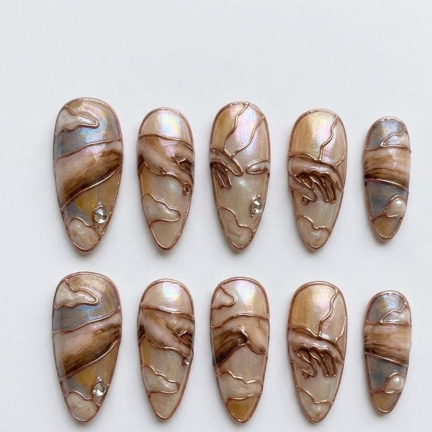 Explore unique nail art inspired by the Renaissance era, featuring hands reaching out and swirled cloud patterns. These stiletto-shaped press-on nails have an iridescent pearlescent finish and detailed copper outlines.