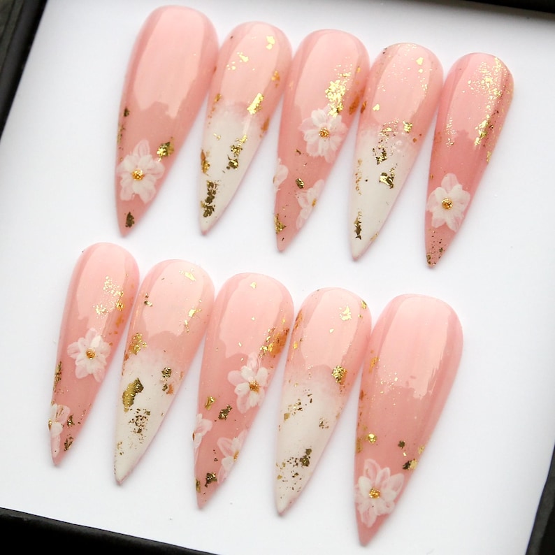Close-up of professional-grade glue-on nails featuring floral designs and gold flakes.