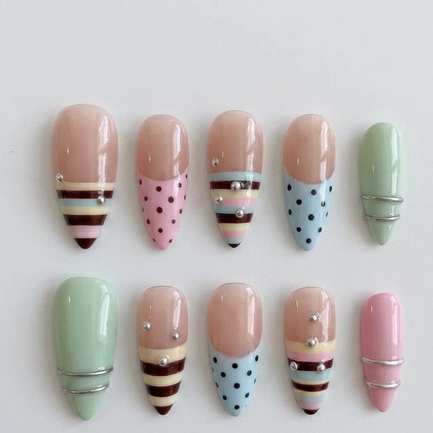 Close-up of elegant stiletto-shaped reusable false nails decorated with a mix of multi-colored circus stripes, mint green, blush pink, and delicate silver crystal clusters.