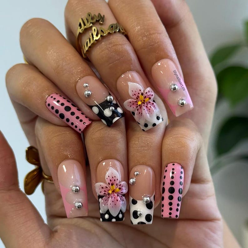 Glossy nude press on nails with 3D pink lilies, black white polka dots, and silver studs for everyday style