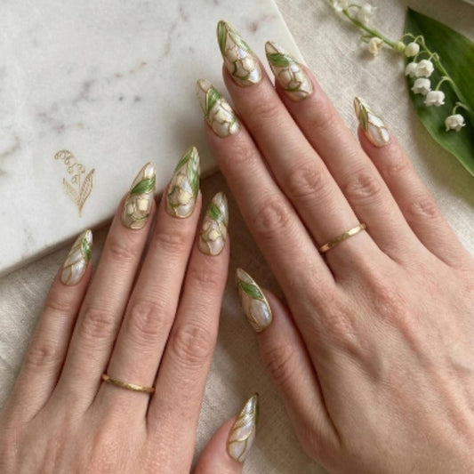 High-resolution image of custom reusable nails on a soft white background, displaying an opulent pearl finish, metallic gold borders, and delicate bell flower patterns.