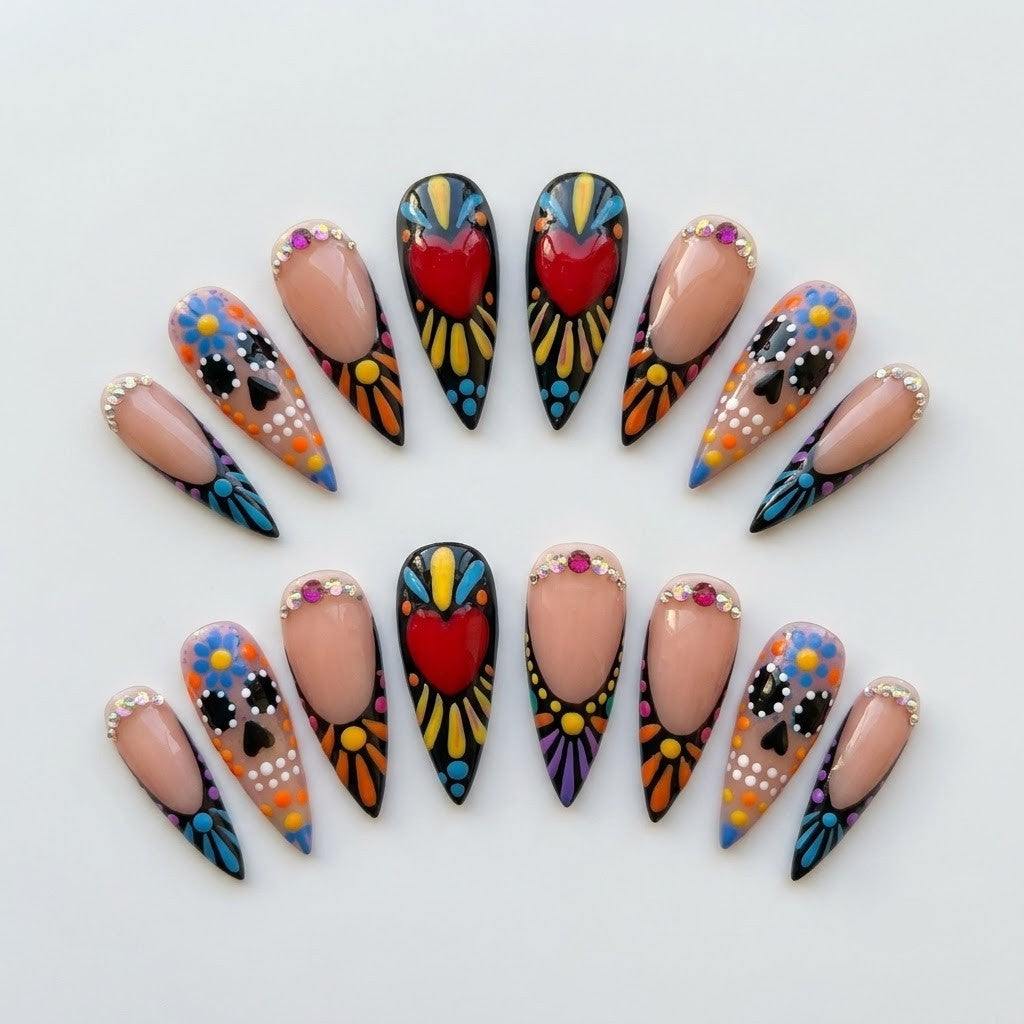 Close-up of handmade false nails showing a mix of glossy black bases with intricate folk-art dotting, crystal rhinestones along the cuticles, and detailed calavera skull illustrations.