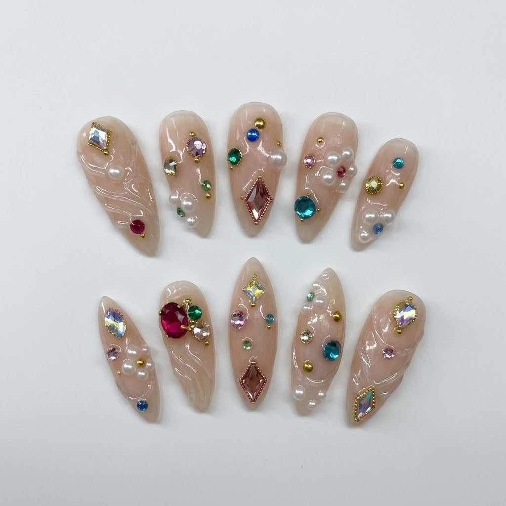 Close-up of handmade maximalist false nails showcasing dimensional clear gel swirls, vibrant sapphire blue, ruby red, and emerald green rhinestones, alongside miniature pearl clusters and gold beads.