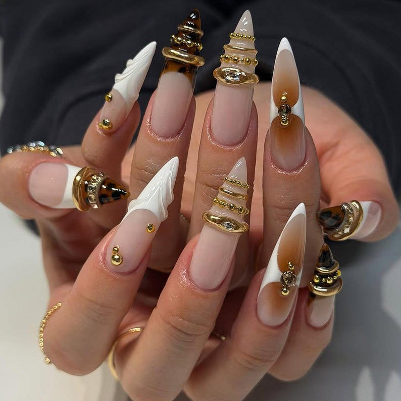 High-fashion hand model pose showing off avant-garde brown tortoiseshell and metallic gold stacked ring press-on nails next to amber crystals.