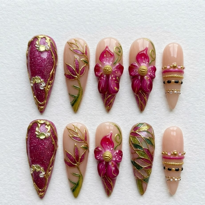A close-up of a bohemian-style manicure featuring sparkling magenta glitter gel fake nails framed with heavy molten gold borders.