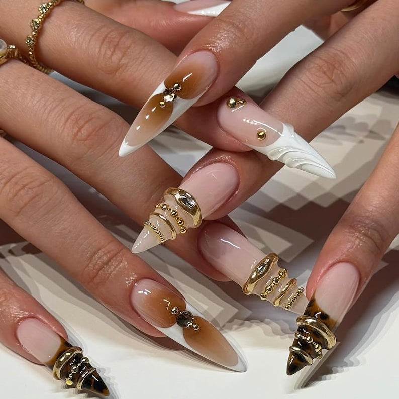 Close-up of hands with decorative nails featuring gold accents on a neutral background