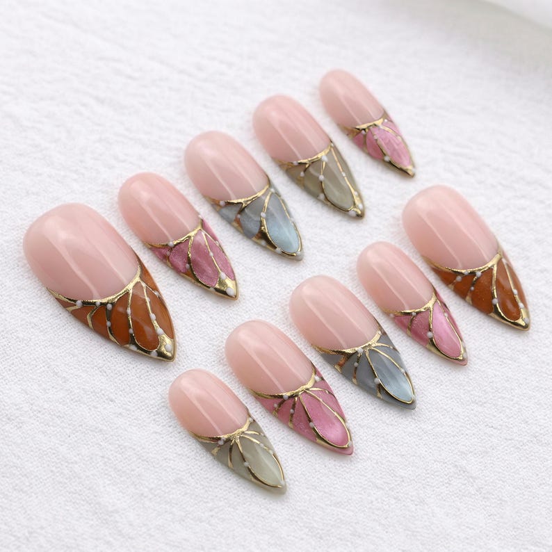 Close-up of nature-inspired nail art designs featuring metallic gold borders and white dots on sharp stiletto-shaped press-ons.