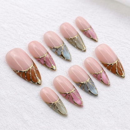 Close-up of nature-inspired nail art designs featuring metallic gold borders and white dots on sharp stiletto-shaped press-ons.
