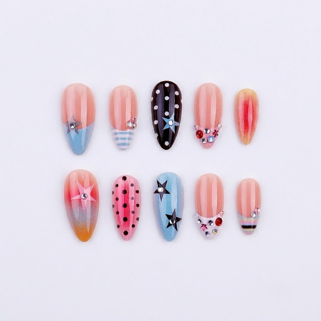A flat lay display of JRNAIL pop-art starburst press-on nails featuring a vibrant mix-and-match design of stars, polka dots, stripes, and rhinestones on a white textured background.