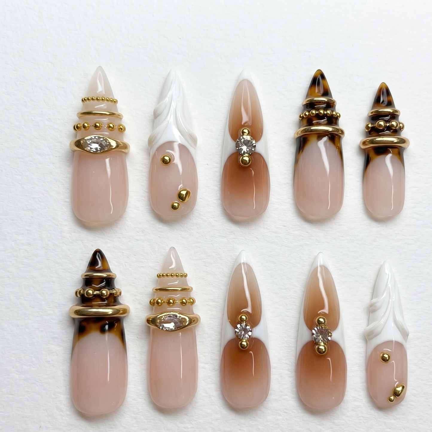 A close-up of an edgy luxury manicure featuring extra-long stiletto fake nails with warm brown gradient ombré and sparkling rhinestone centers.