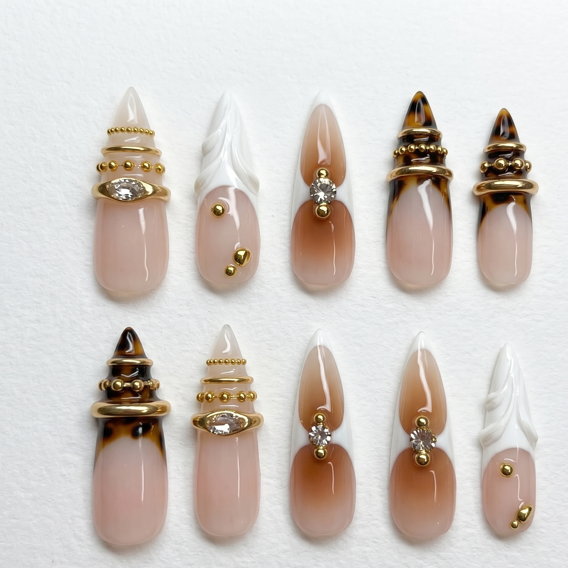 A close-up of an edgy luxury manicure featuring extra-long stiletto fake nails with warm brown gradient ombré and sparkling rhinestone centers.